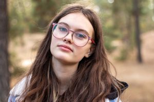 Close up portrait of a beautiful girl in glasses on a blurred green background. Hipster teenager in the park.