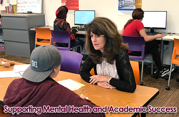 Mary Lynn Wagner of Camino a Casa sits at a table in a classroom speaking to a student.